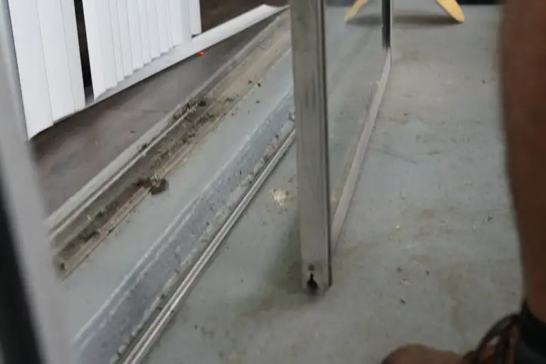 Sliding glass door parts visible at the sill: bottom track, threshold, panel stile and roller